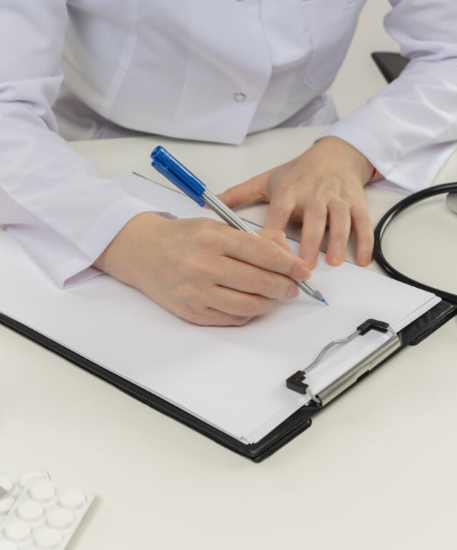 middle-aged female doctor wearing wearing medical robe with stethoscope sitting at desk work on laptop with medical tools write on clipboard on isolated white backgroung with copy space middle-aged female doctor wearing wearing medical robe with stethoscope sitting at desk work on laptop with medical tools write on clipboard on isolated white backgroung with copy space