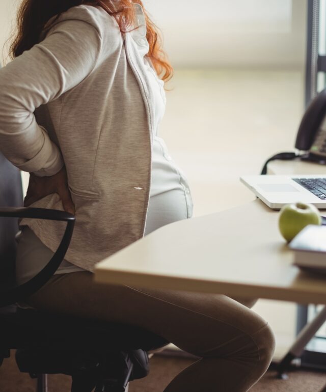 empresaria-embarazada-sosteniendo-su-espalda-mientras-esta-sentado-en-una-silla empresaria-embarazada-sosteniendo-su-espalda-mientras-esta-sentado-en-una-silla