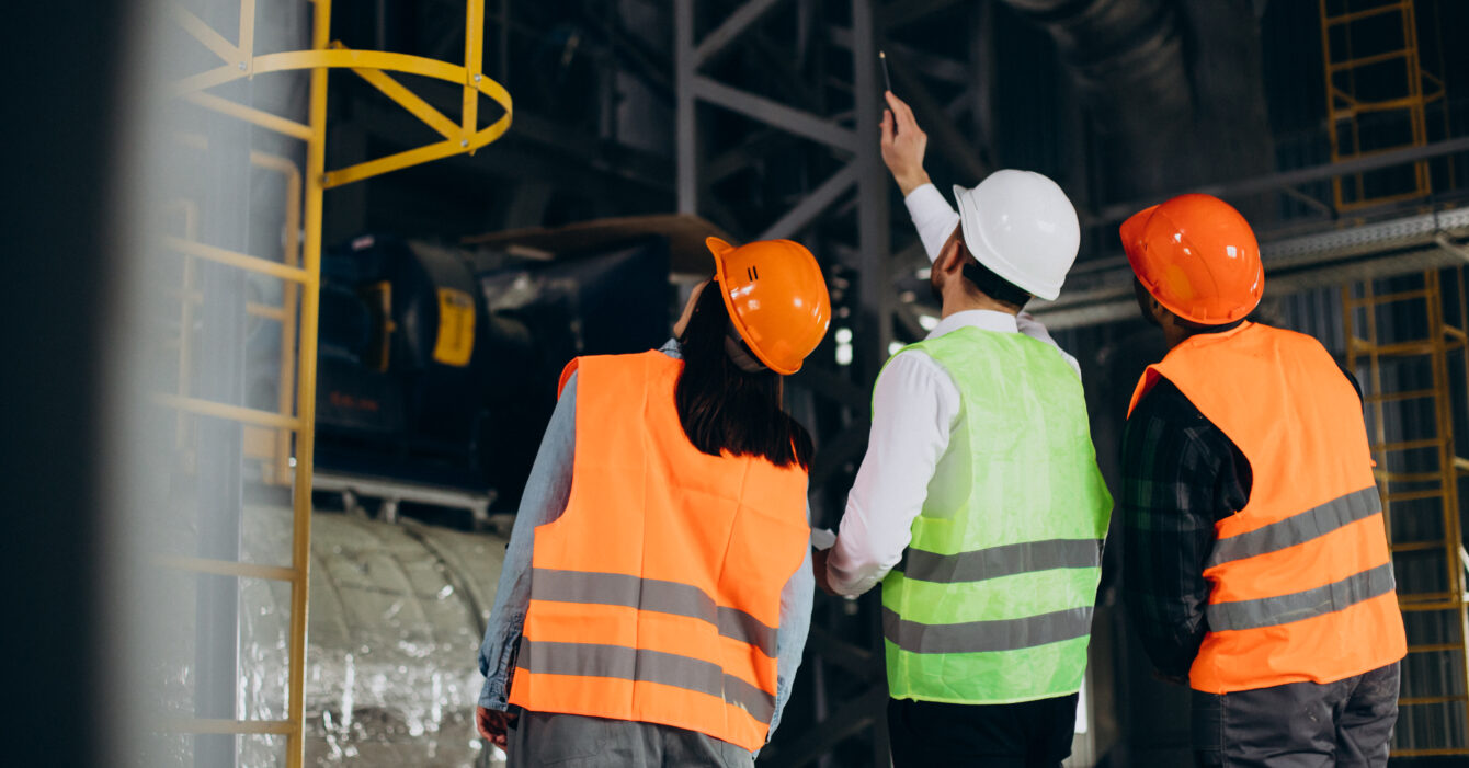 Three factory workers in safety hats discussing manufacture plan