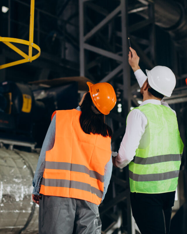 Three factory workers in safety hats discussing manufacture plan